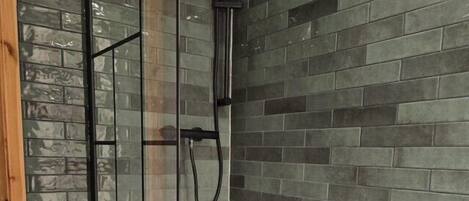 A bathroom with a glass-enclosed shower, a white bathtub, and a tiled wall with a brick pattern.
