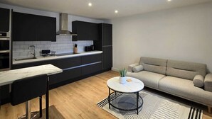A modern kitchen with dark cabinetry, a marble countertop, and a round coffee table with a plant. - Nairn Nights (Nairn)