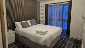 A modern bedroom with a bed, bedside tables, a window with curtains, and a patterned floor. - Nairn Nights (Nairn)