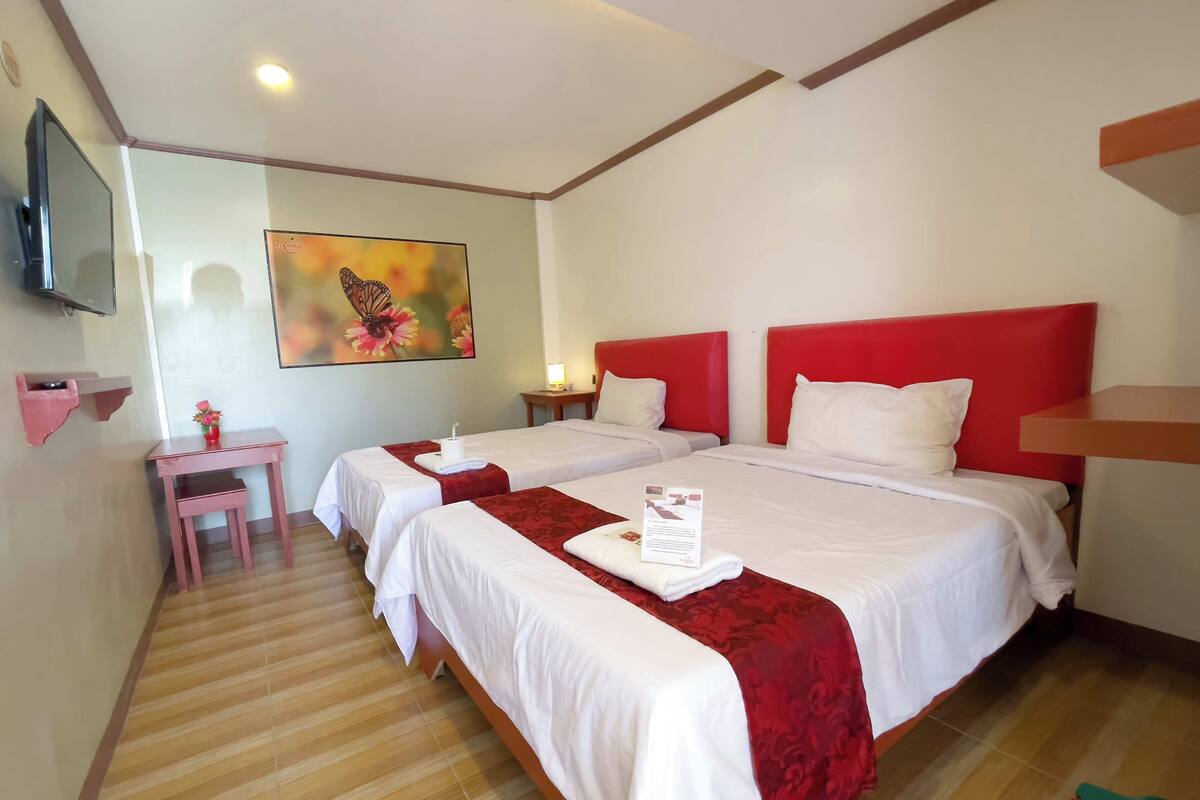 A hotel room with two beds, a small desk, a TV, and a painting on the wall.