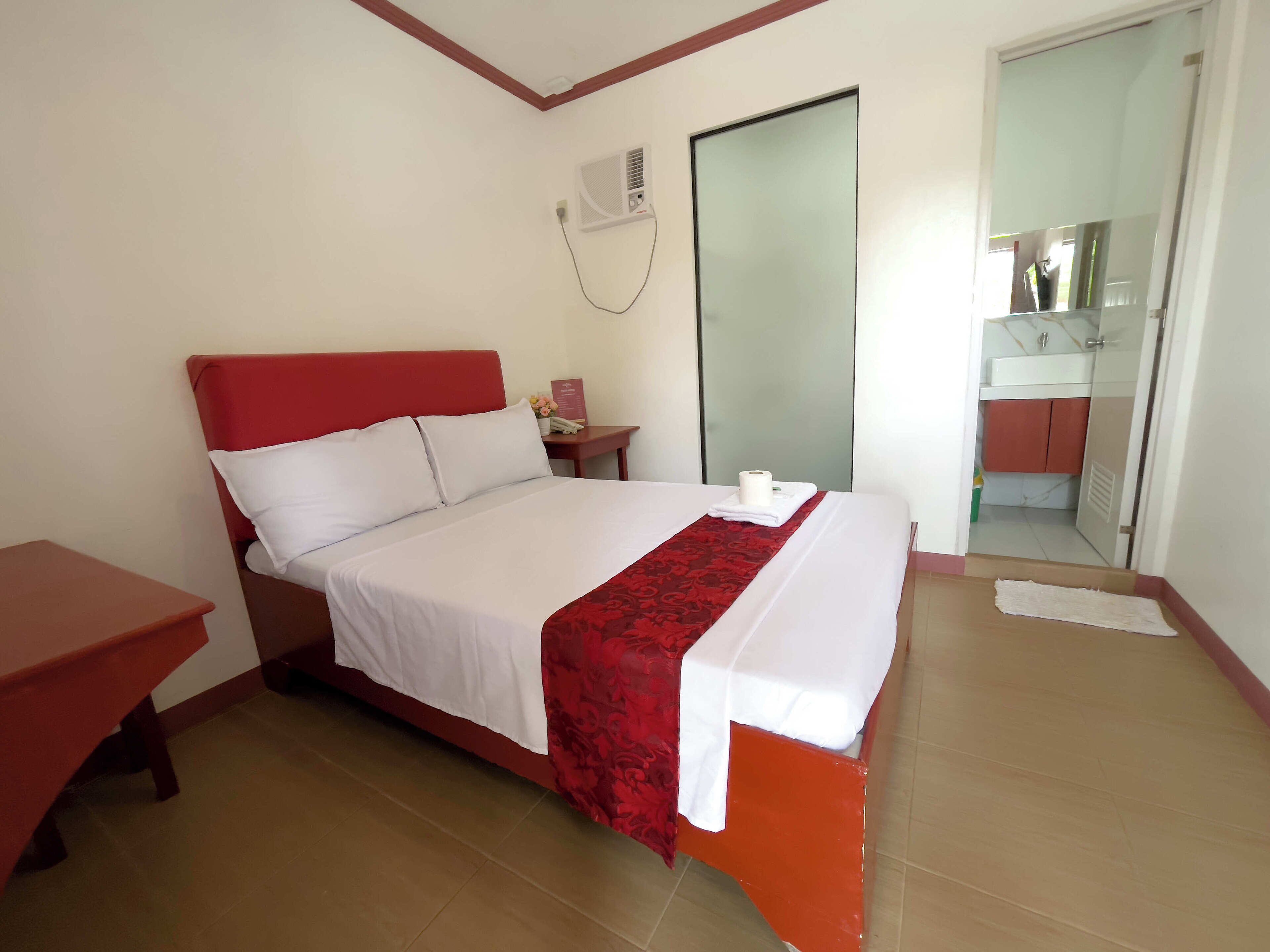 Una habitación de hotel con una cama, una mesita de noche, un espejo y un baño visible a través de una puerta abierta.