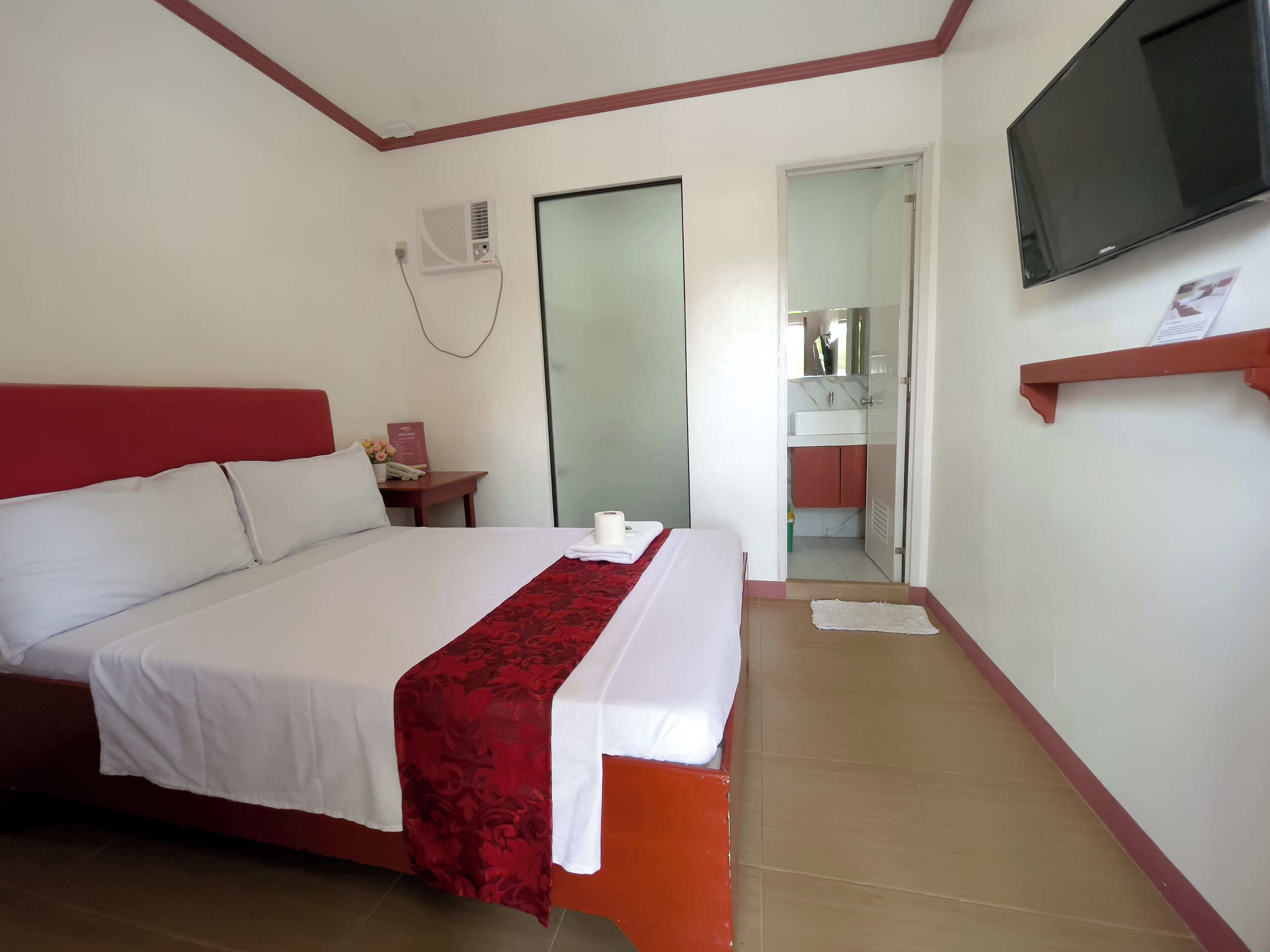 Une chambre d’hôtel avec un lit, une télévision, une salle de bain visible à travers une porte ouverte et un mur d’accent de couleur rouge.