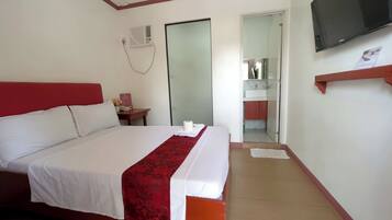 Une chambre d’hôtel avec un lit, une télévision, une salle de bain visible à travers une porte ouverte et un mur d’accent de couleur rouge.