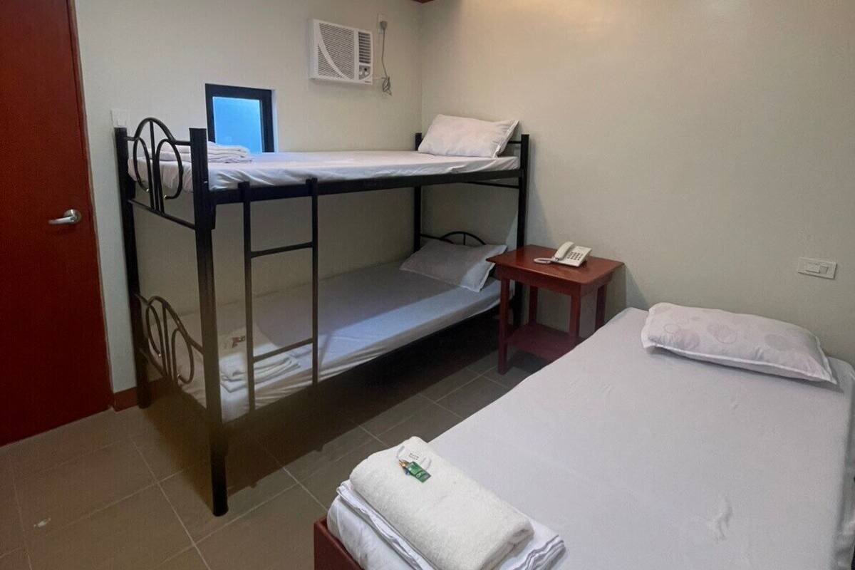 A dormitory room with bunk beds, a desk, a telephone, and a wall-mounted air conditioner.