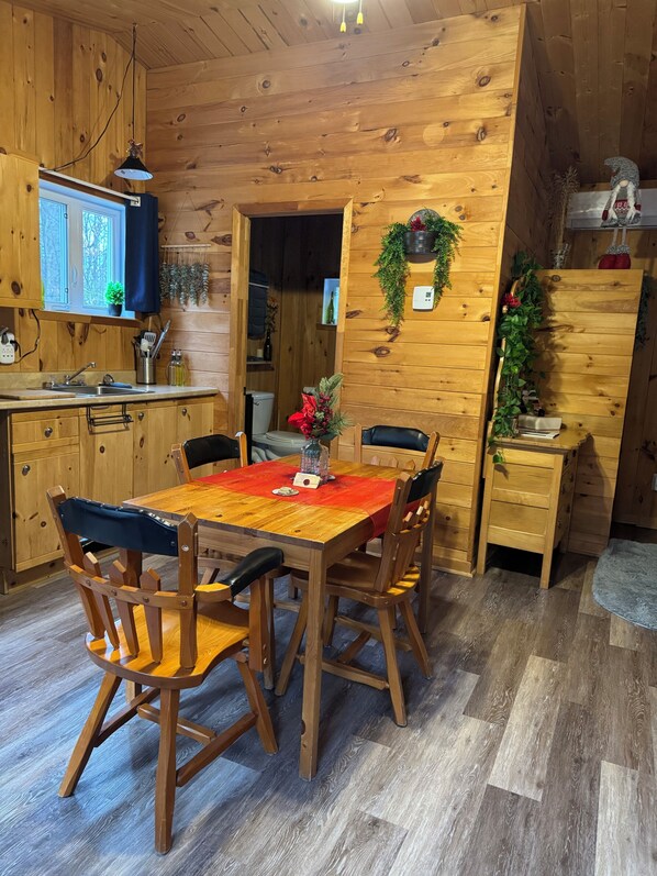 A wooden interior with a dining table, chairs, a kitchen area, and a small plant.