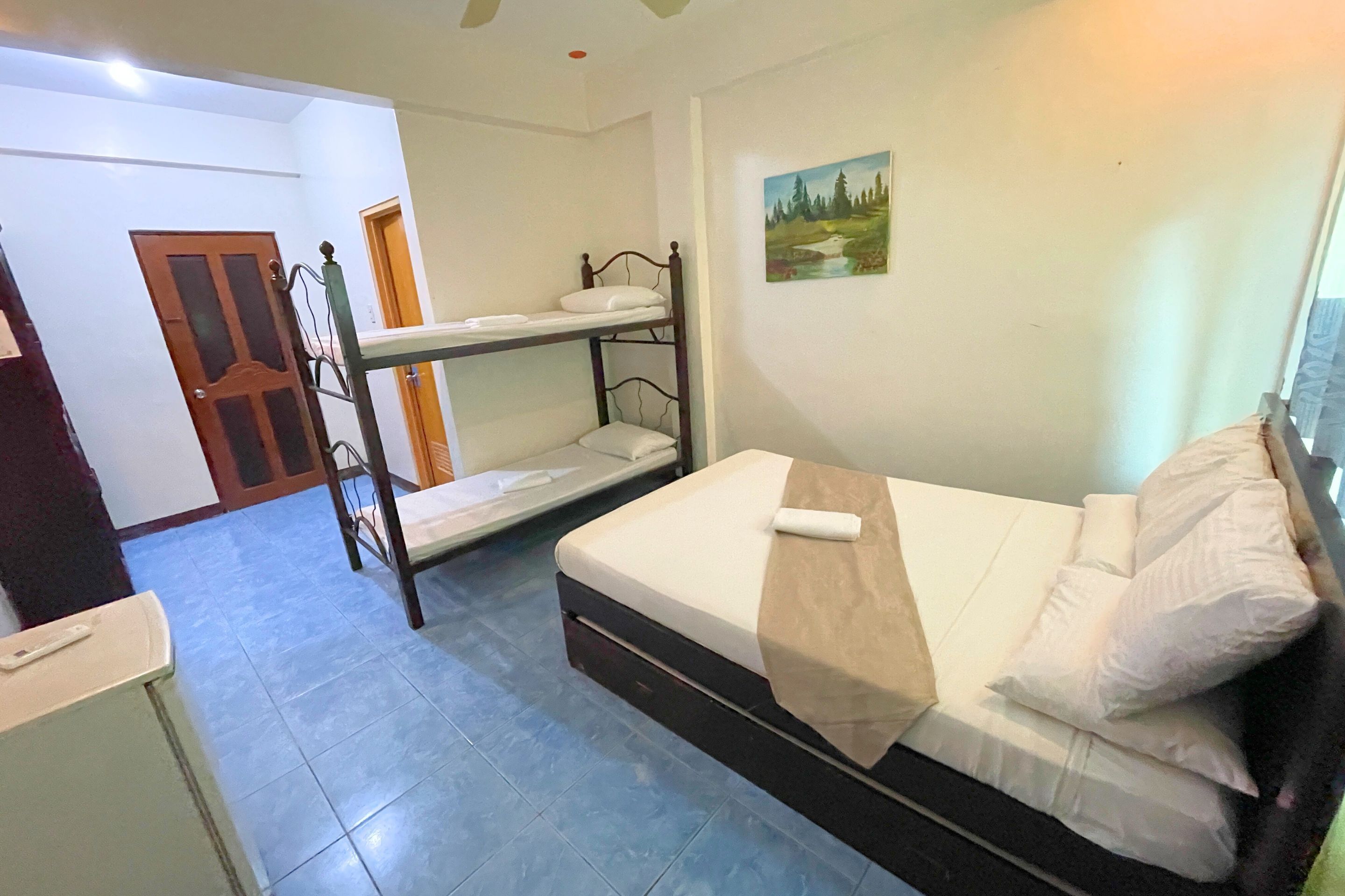 Una habitación con literas, una cama individual, un cuadro en la pared y una puerta.