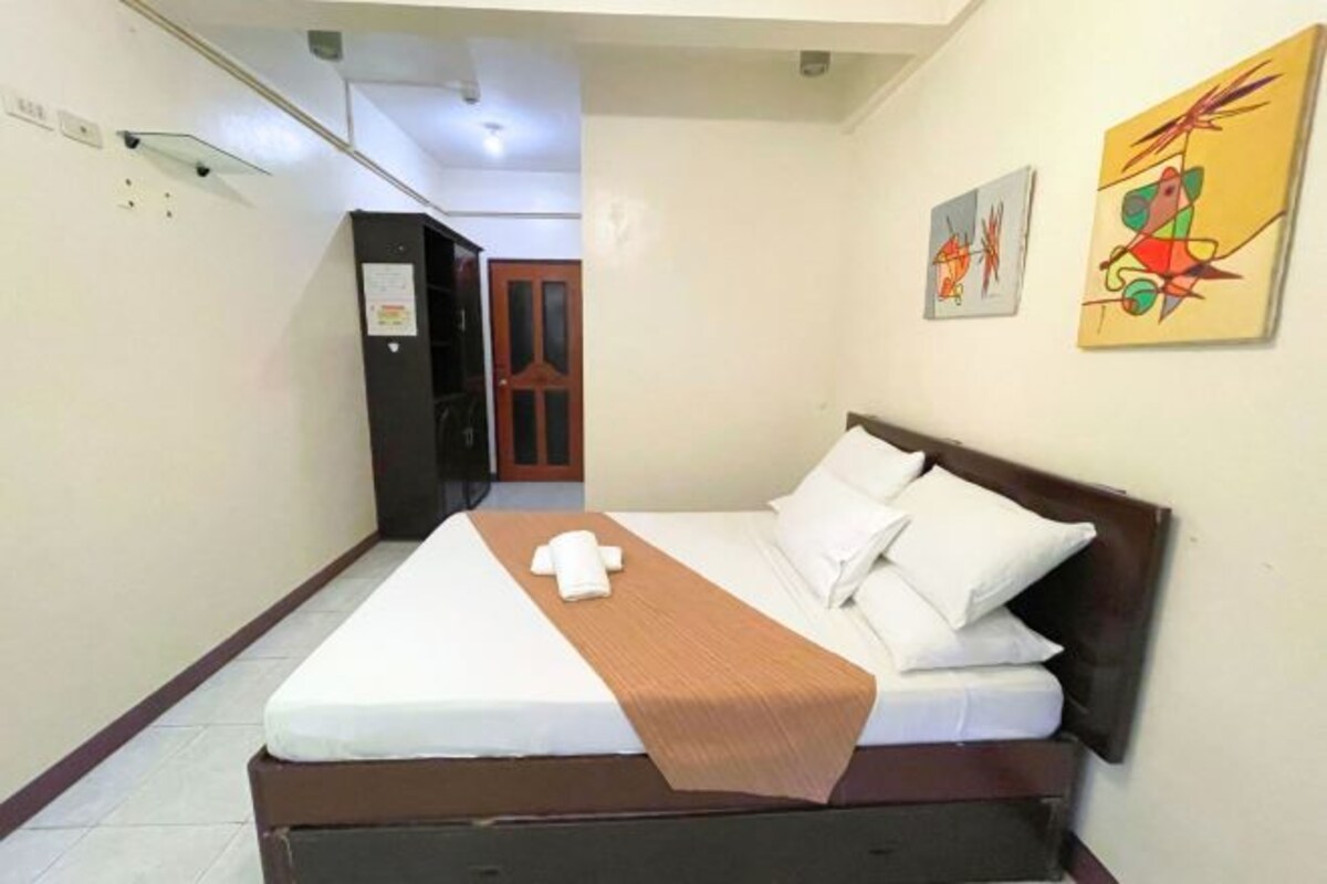 Una habitación de hotel con una cama, cabecero de madera y dos cuadros en la pared.