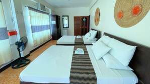 Habitación de hotel con dos camas, un ventilador de pie, una ventana con cortinas y un adorno en la pared.