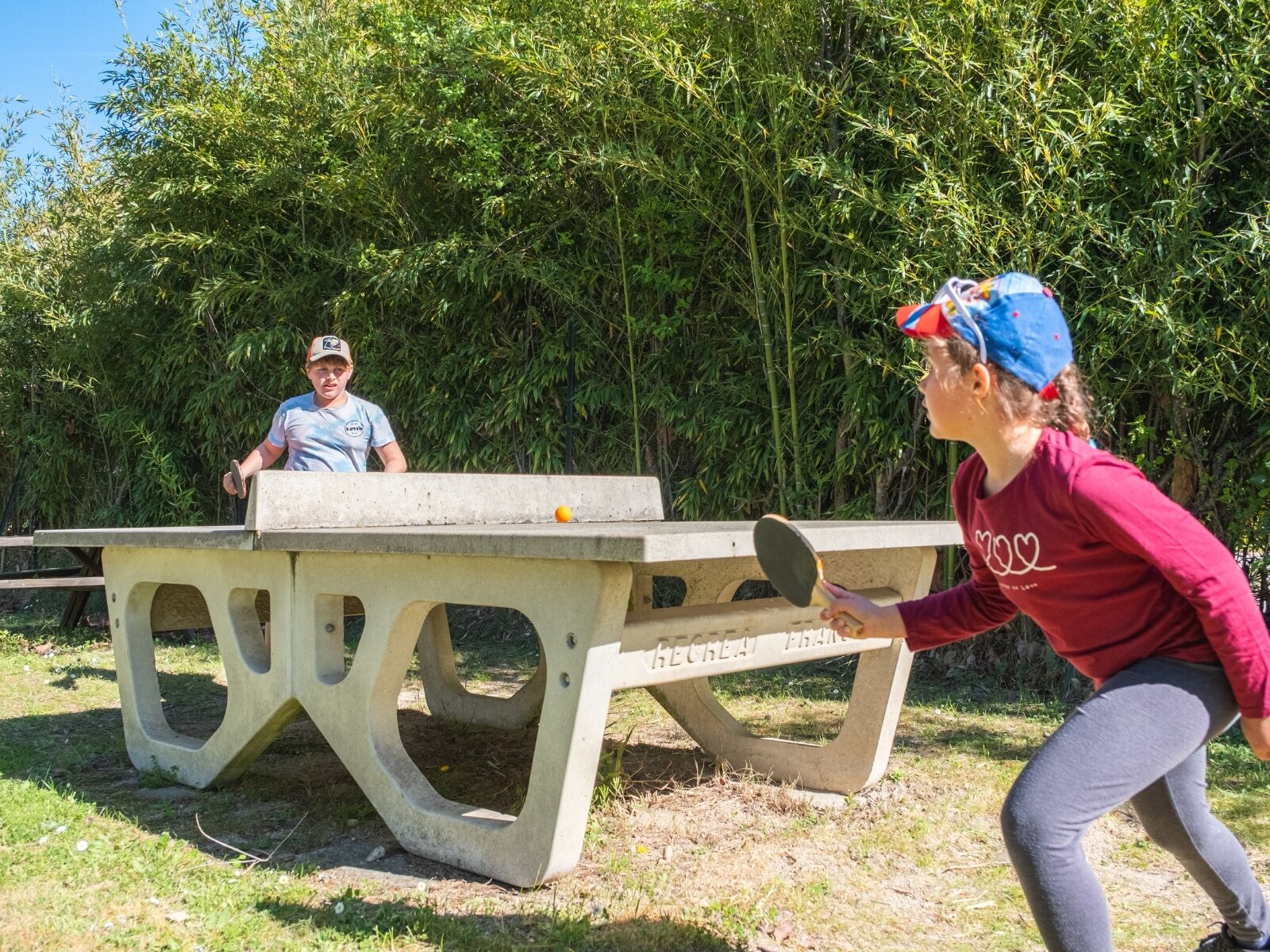 A concrete table with 'HECREAT FRANK' written on it, surrounded by greenery.