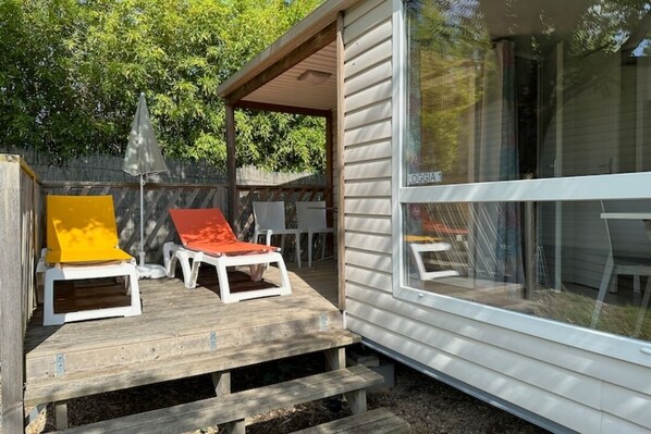 A wooden deck with two lounge chairs, one yellow and one red, and a covered patio area. - Camping Pegomas (St.-Remy-de-Provence)