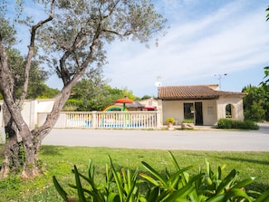 A small building with a tiled roof, a fenced area with colorful decorations, and a tree in the foreground.