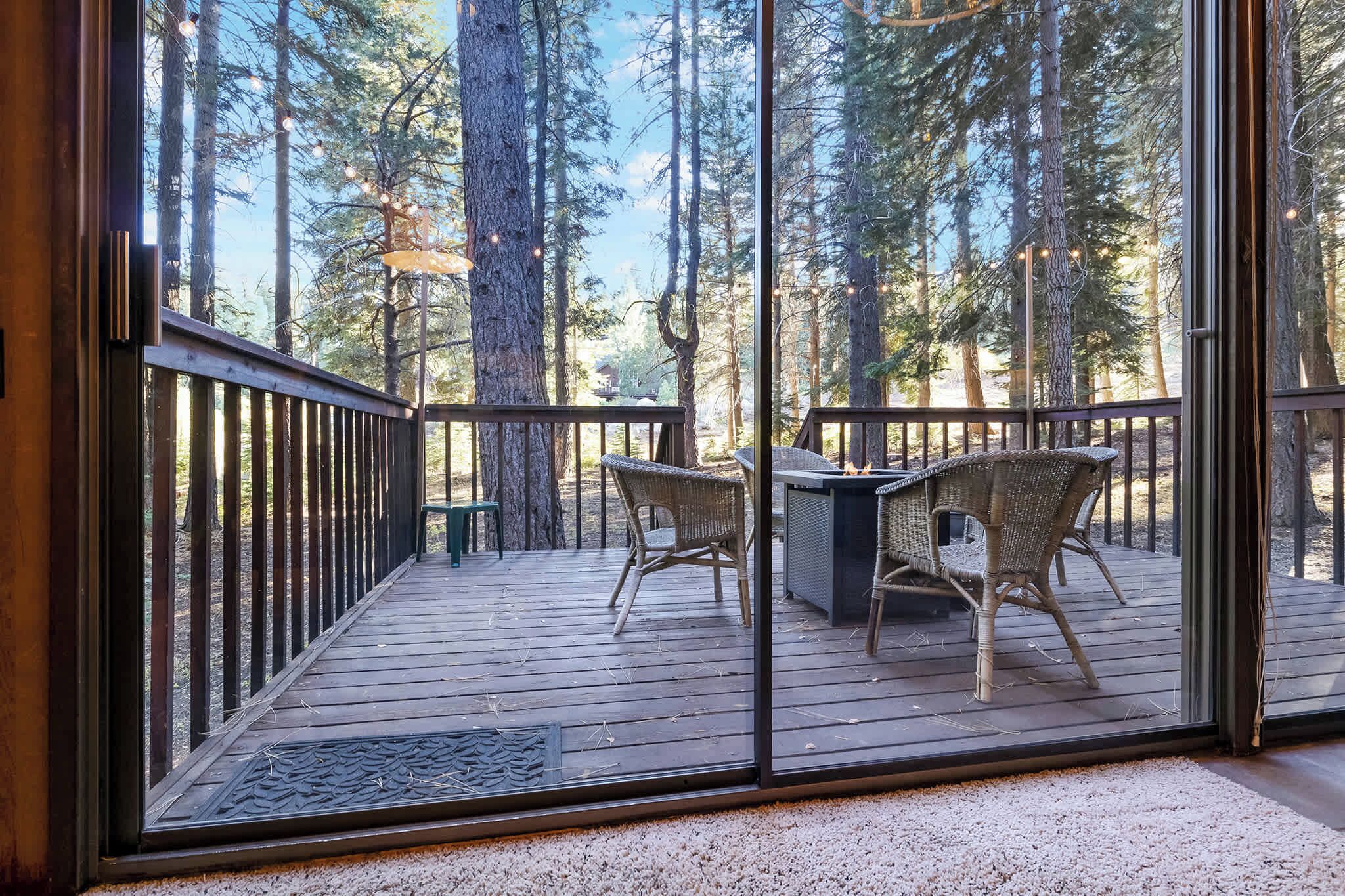 A wooden deck with wicker chairs and a table, overlooking a forest with tall trees.