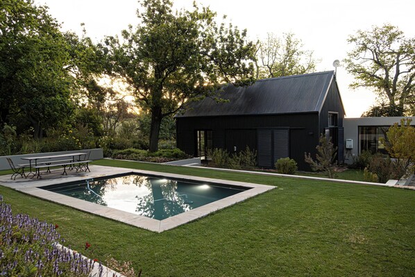 Ein modernes Haus mit Swimmingpool, einer Terrasse mit Tisch und Stühlen sowie einem gepflegten Rasen.