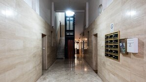Un pasillo con suelo de mármol, una escalera y un buzón de seguridad en la pared.