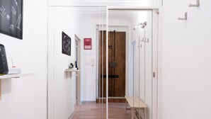 Un pasillo con una puerta de madera, un banco y un estante con un dispositivo.