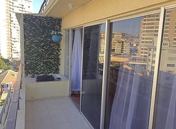 A balcony with a view of a cityscape, a potted plant, and a sliding glass door.