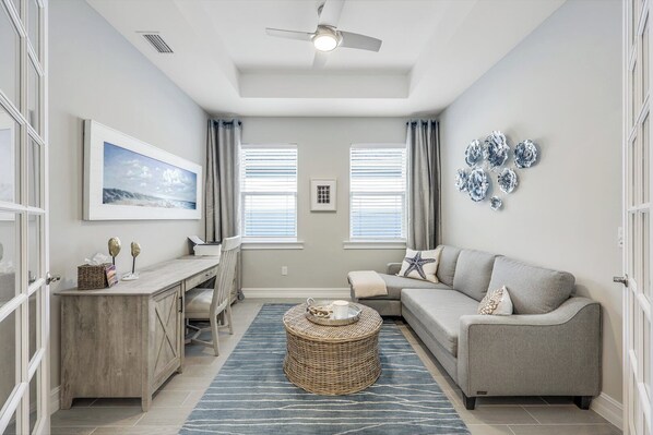 A modern living room with a gray sofa, a coffee table, and a dining area with a wooden table and chairs. - Seasons at Bonita (Bonita Springs)