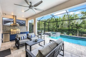 A modern outdoor kitchen with a built-in grill, a seating area with a sofa and chairs, and a pool with a hot tub. - Seasons at Bonita (Bonita Springs)