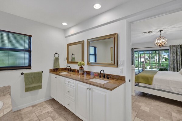 Un baño moderno con tocador doble, un espejo grande y vista al dormitorio a través de una puerta abierta.