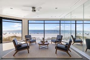 Une chambre moderne dotée d’une grande fenêtre donnant sur une plage, et aménagée avec des chaises et une table centrale.