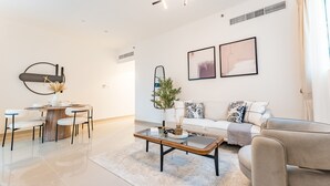 Een moderne woonkamer met een bank, salontafel en stoelen. Er hangen kunstwerken aan de muur en staat een plant.