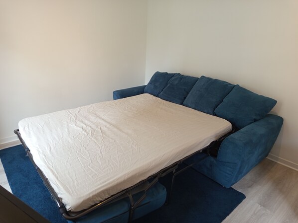 A compact bed with a mattress and blue upholstered headboard in a room with a light-colored wall and wooden flooring. - Quiet, comfortable and conveniently located (Nice)