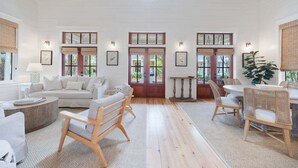 Una habitación amplia con techo alto, ventanas grandes, un comedor con sillas de mimbre y una zona de estar acogedora con sofá y sillones.