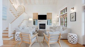 Un amplio salón con chimenea, sofás blancos, sillas de madera y una escalera.