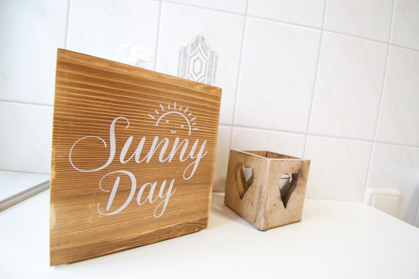 Un letrero de madera con la inscripción 'Sunny Day', colocado junto a una caja de madera con formas de corazón recortadas.