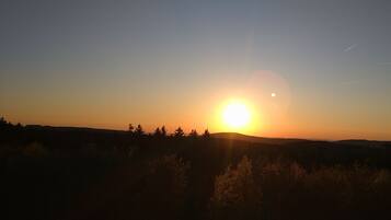 Um pôr do sol sobre uma paisagem acidentada, com árvores recortadas no céu.