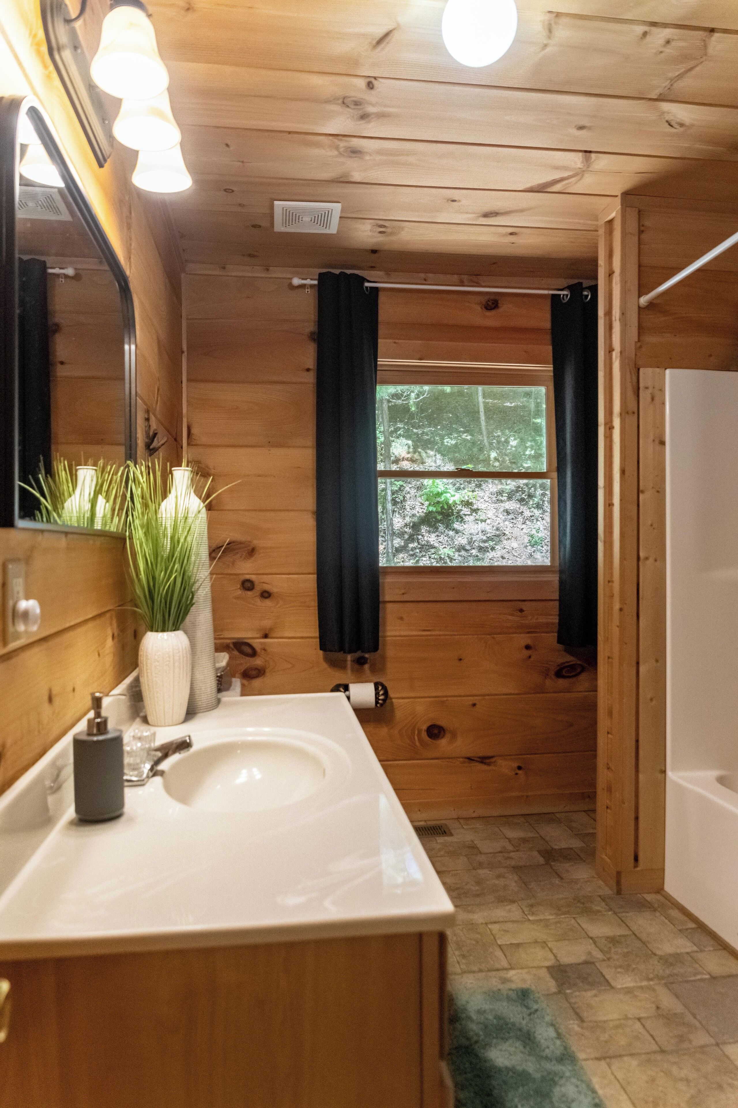 Une salle de bain rustique, aménagée dans une cabane en bois, avec un lavabo, un miroir et une fenêtre.