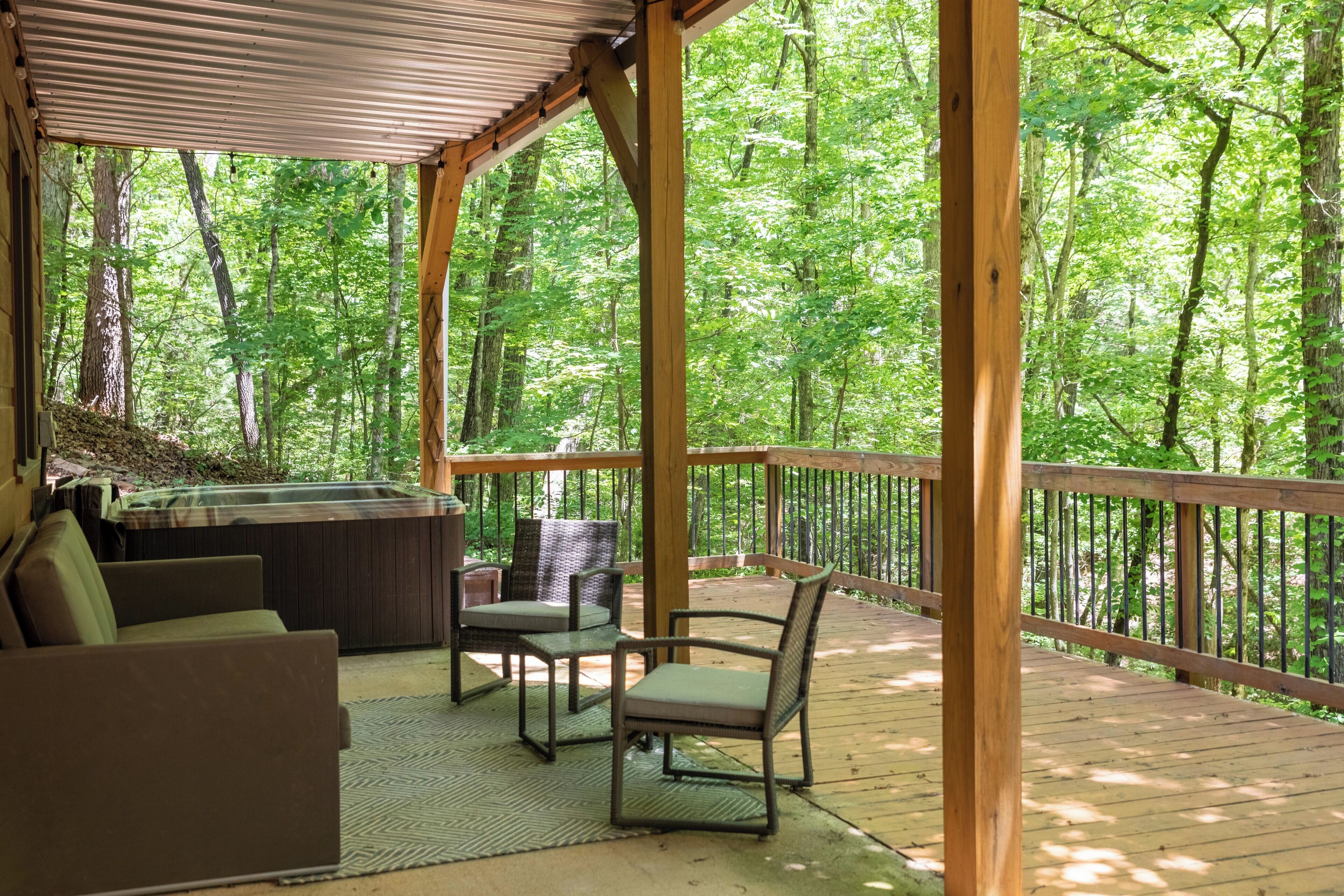 Um deck de madeira com mobiliário externo e banheira de hidromassagem, cercado por uma área arborizada.