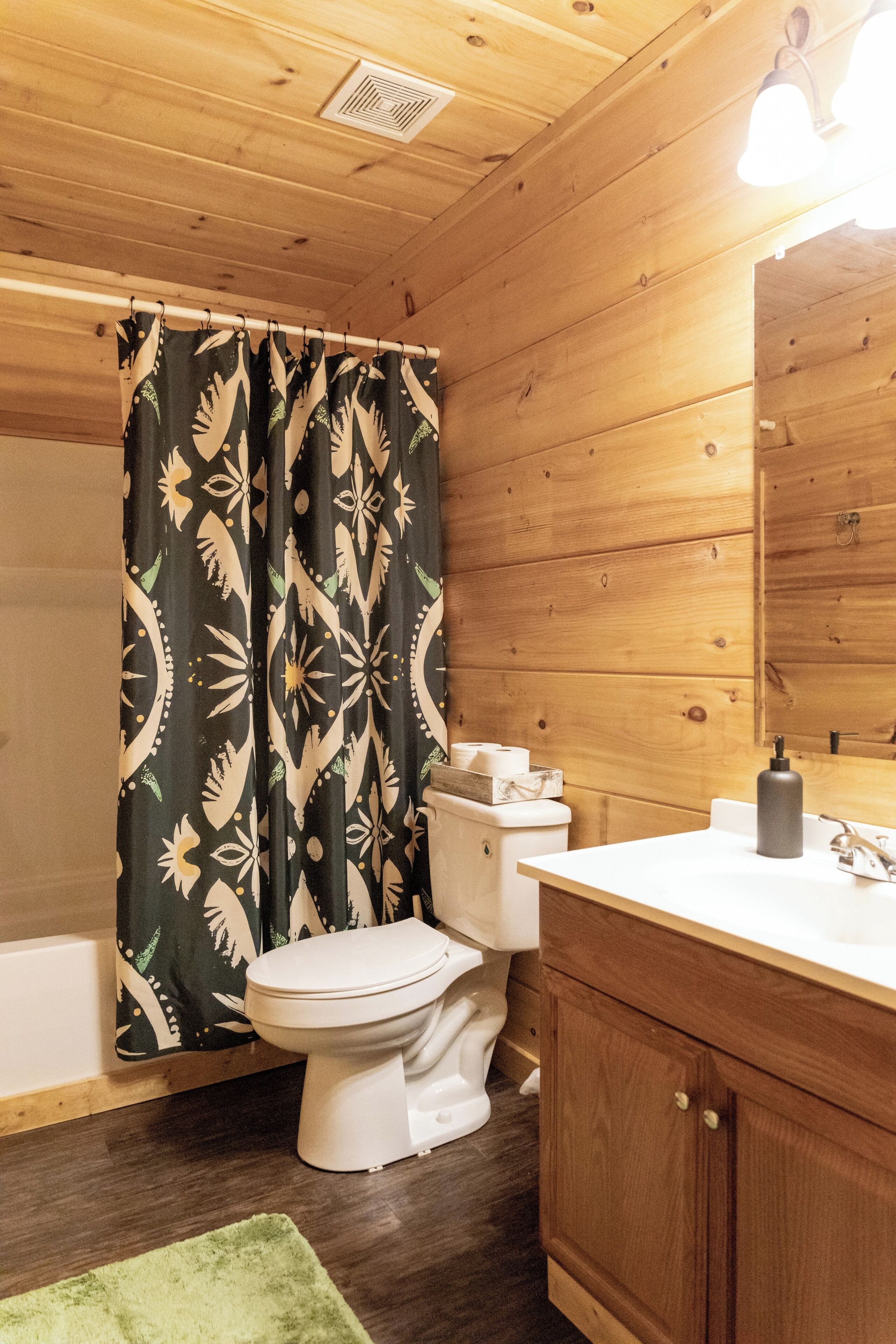 A wooden cabin bathroom with a toilet, sink, and shower curtain.