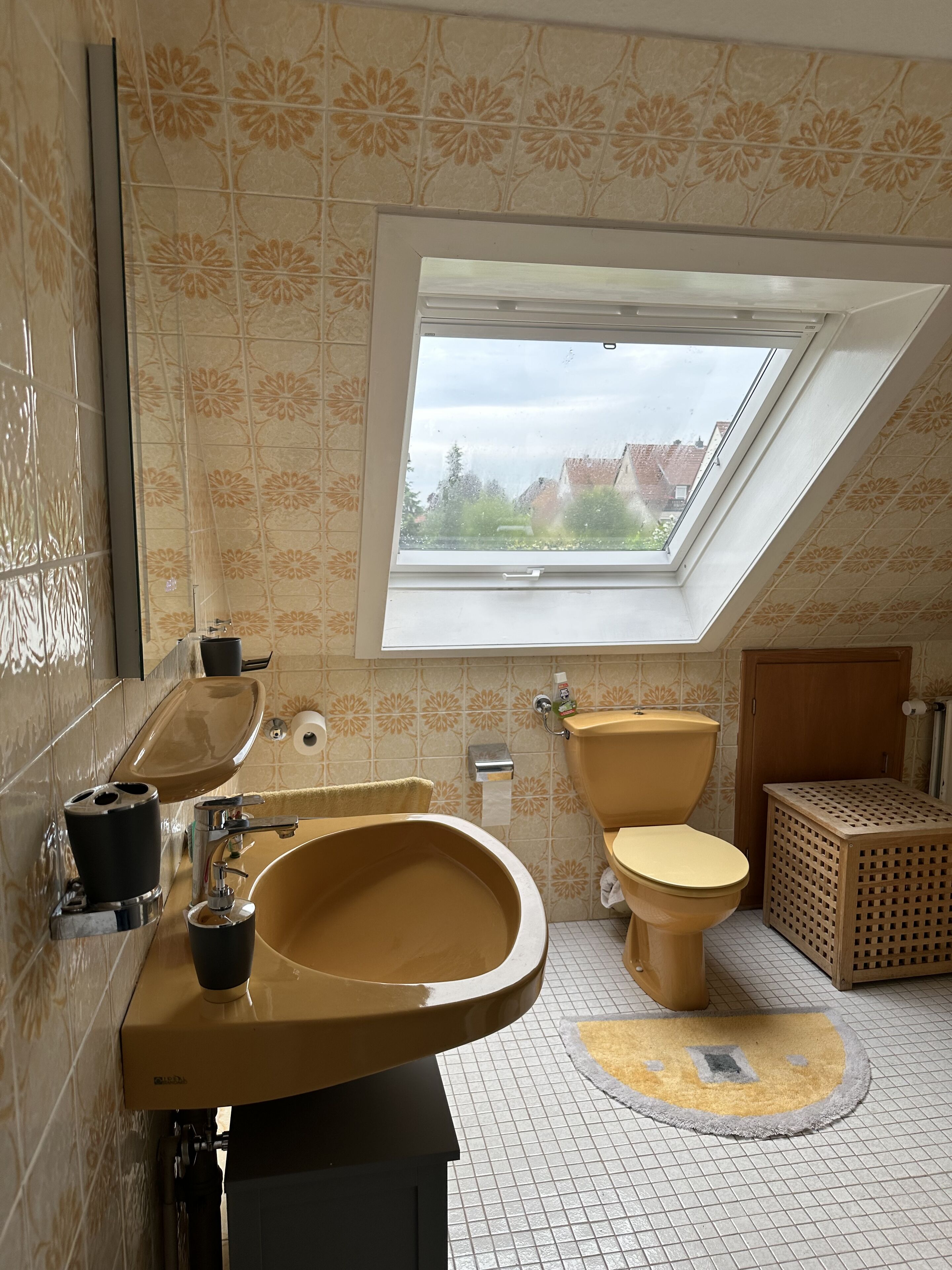 Ein Badezimmer mit Dachfenster, einem Waschbecken, einer Toilette und einem kleinen Wäschekorb.