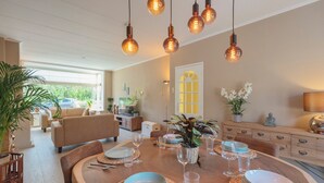 Et spiseområde med et træbord dækket til seks personer, omgivet af stole. Der hænger lysekranser over bordet.