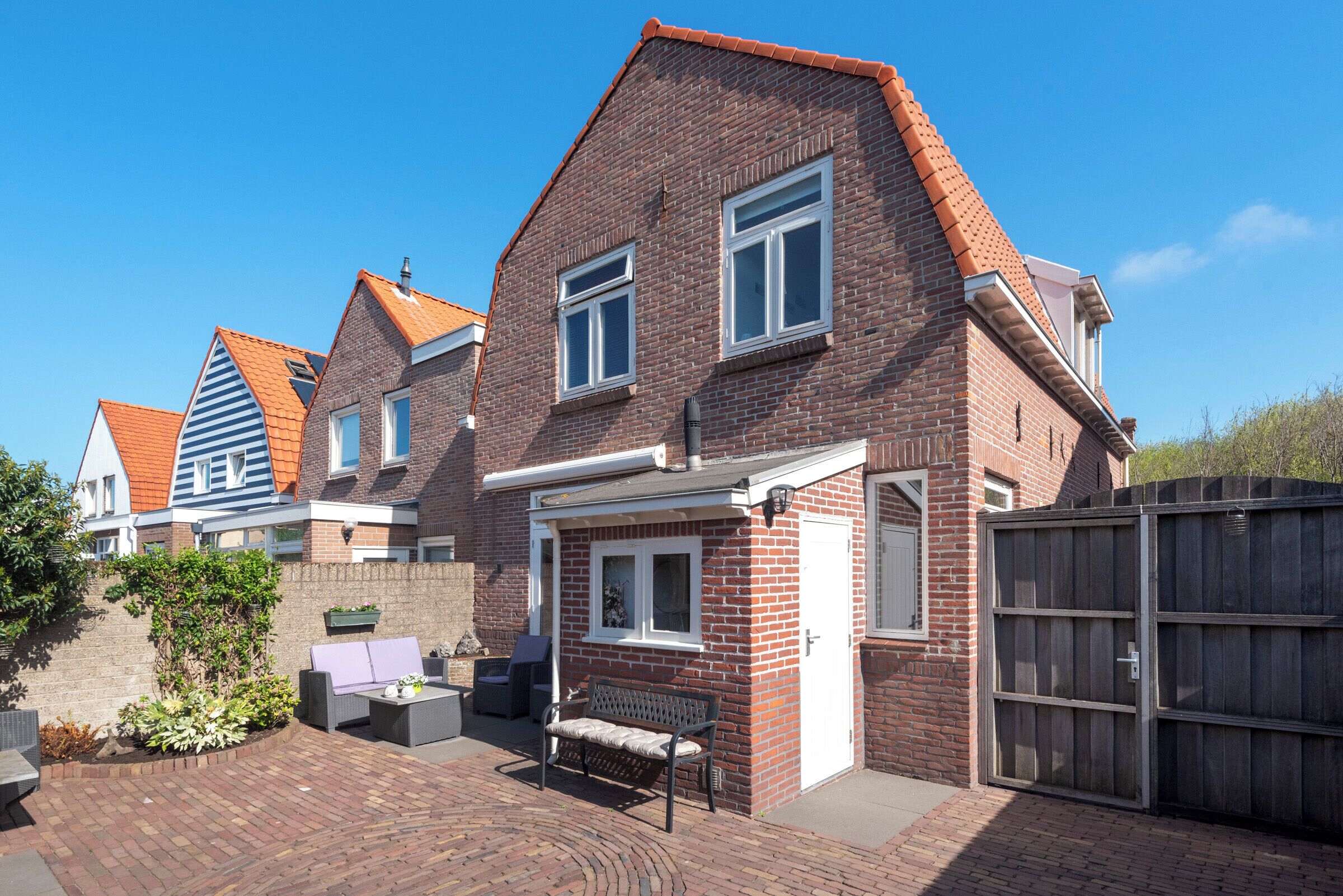 A row of brick houses with a shared driveway, a bench, and a gated entrance.