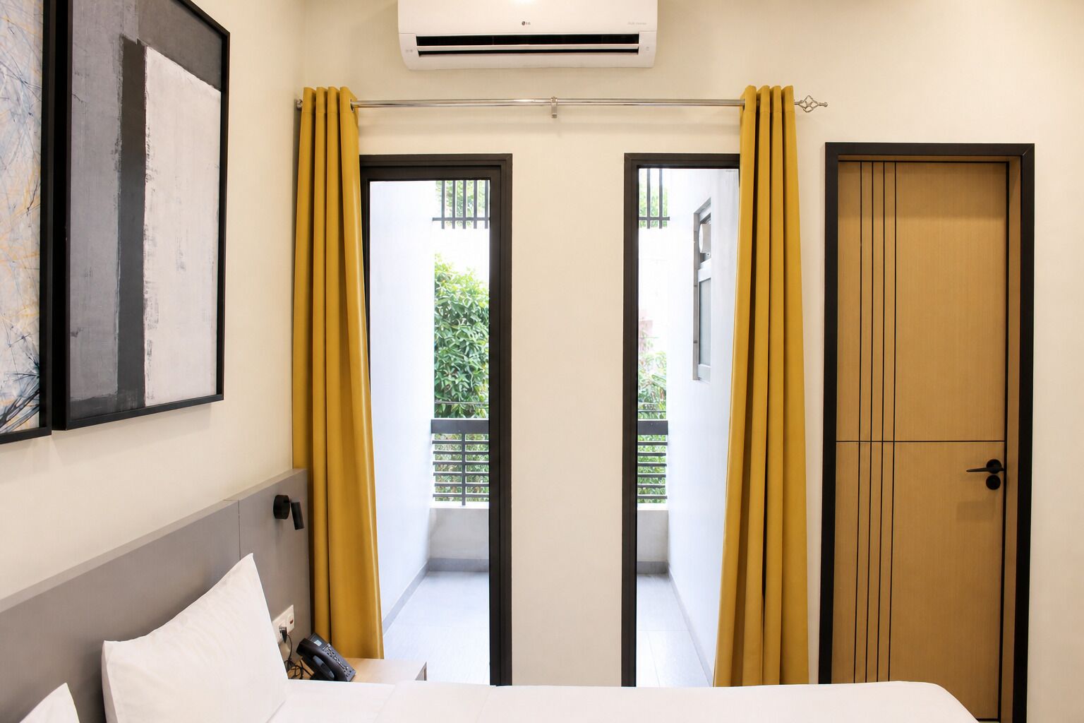 A hotel room with a bed, a telephone, a painting, and a door leading to a balcony.