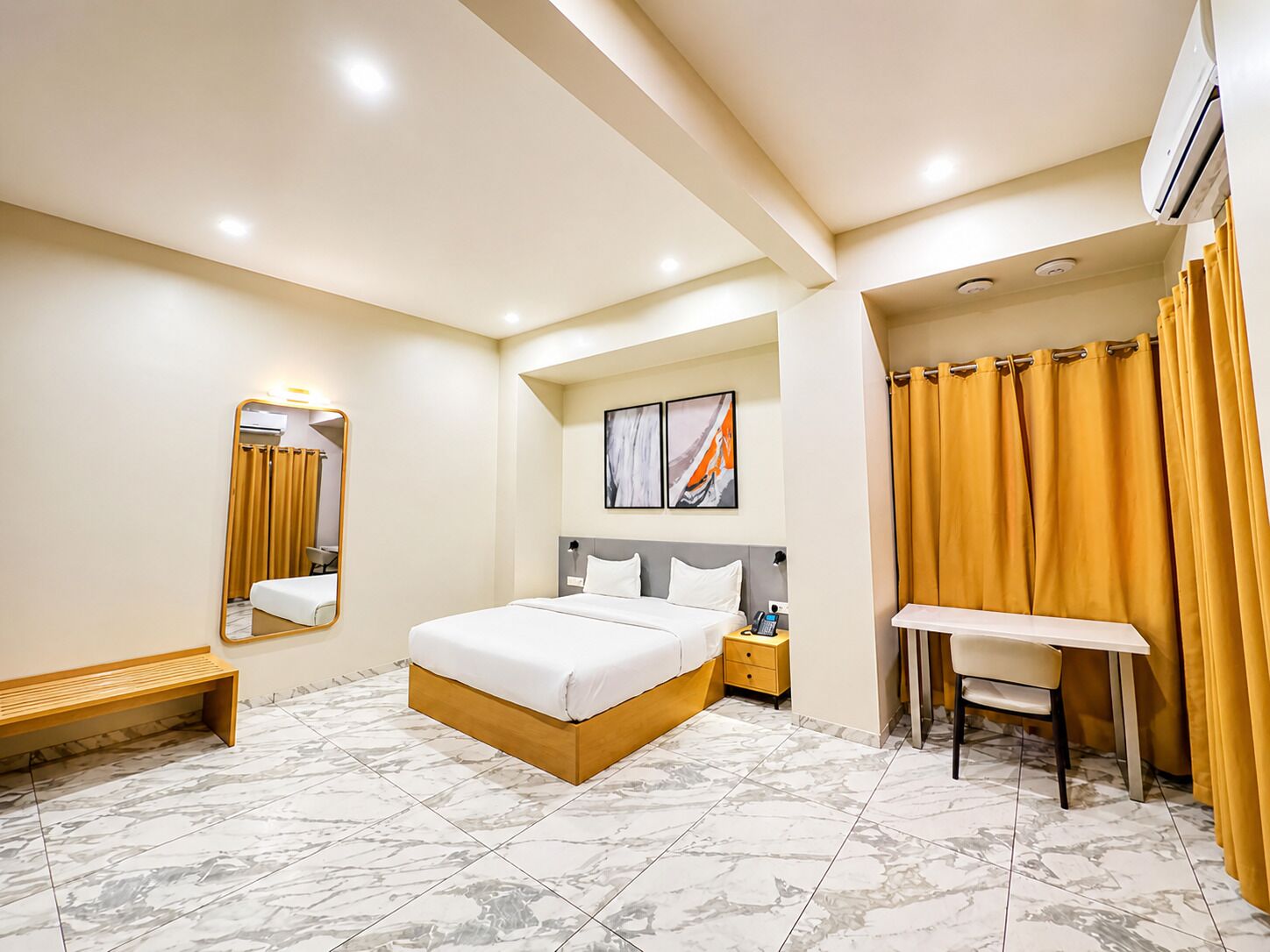 A hotel room with a bed, a desk, a mirror, a bench, and a shower area.