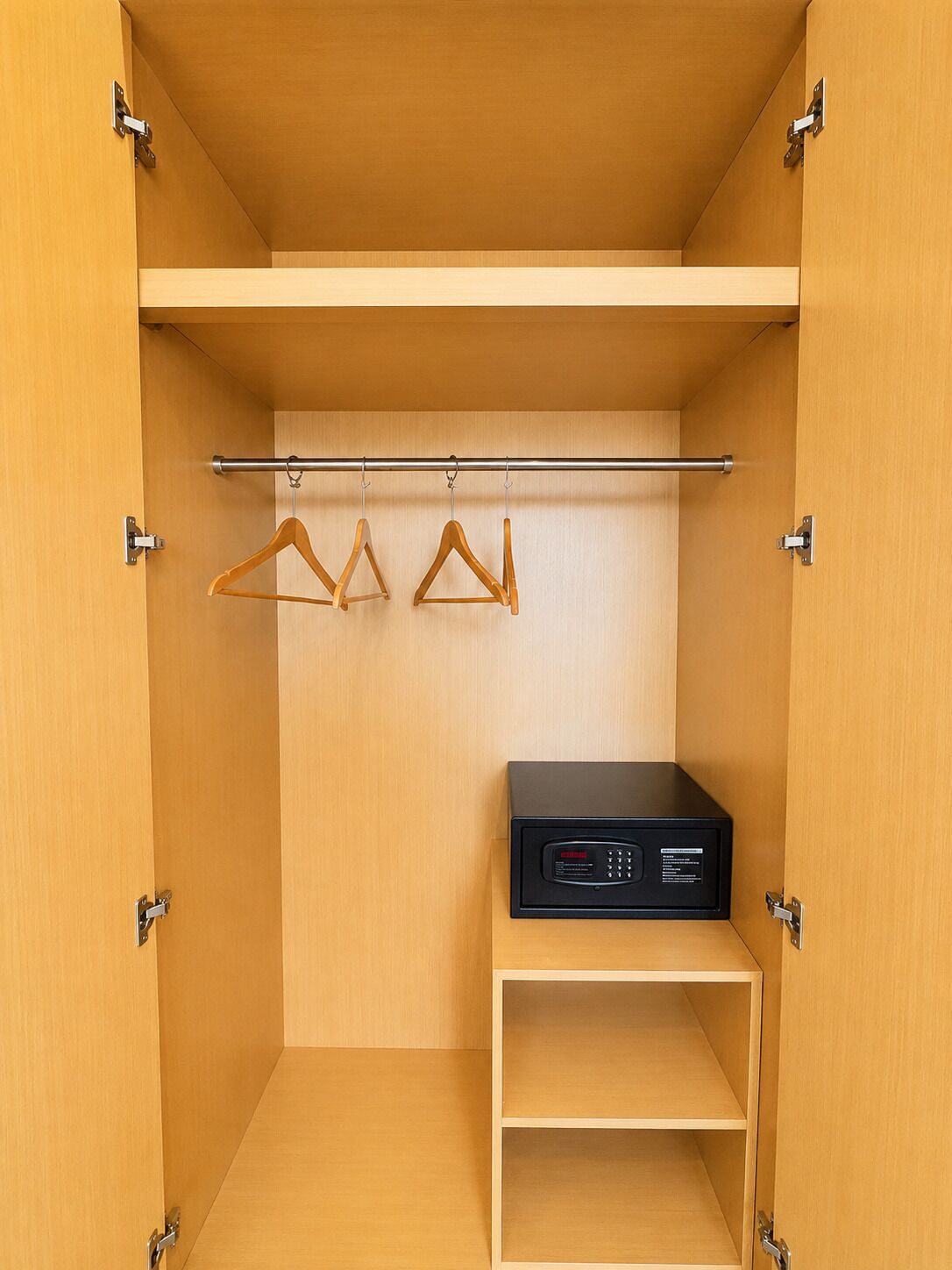 Een kast met een kledingroede, twee houten hangers en een zwart elektronisch apparaat op de onderste plank.