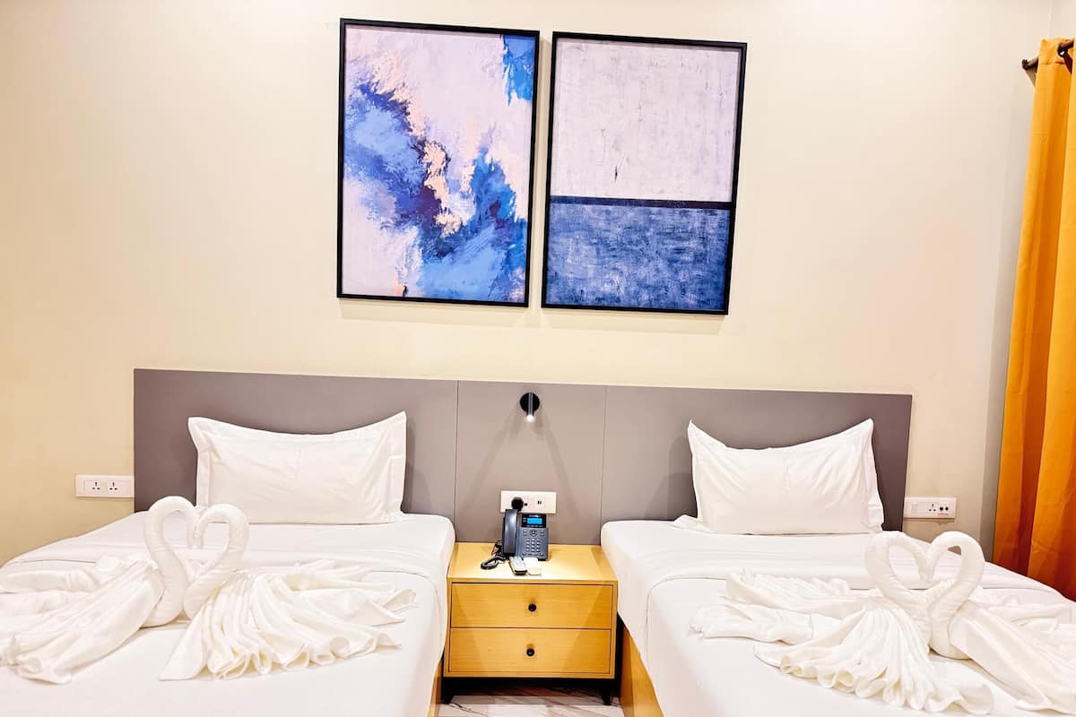 A hotel room with two beds, a nightstand with a phone and a lamp, and abstract art on the wall.