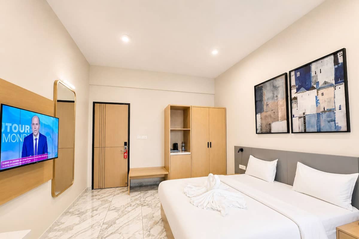 A hotel room with a bed, a TV, a wardrobe, and artwork on the wall.