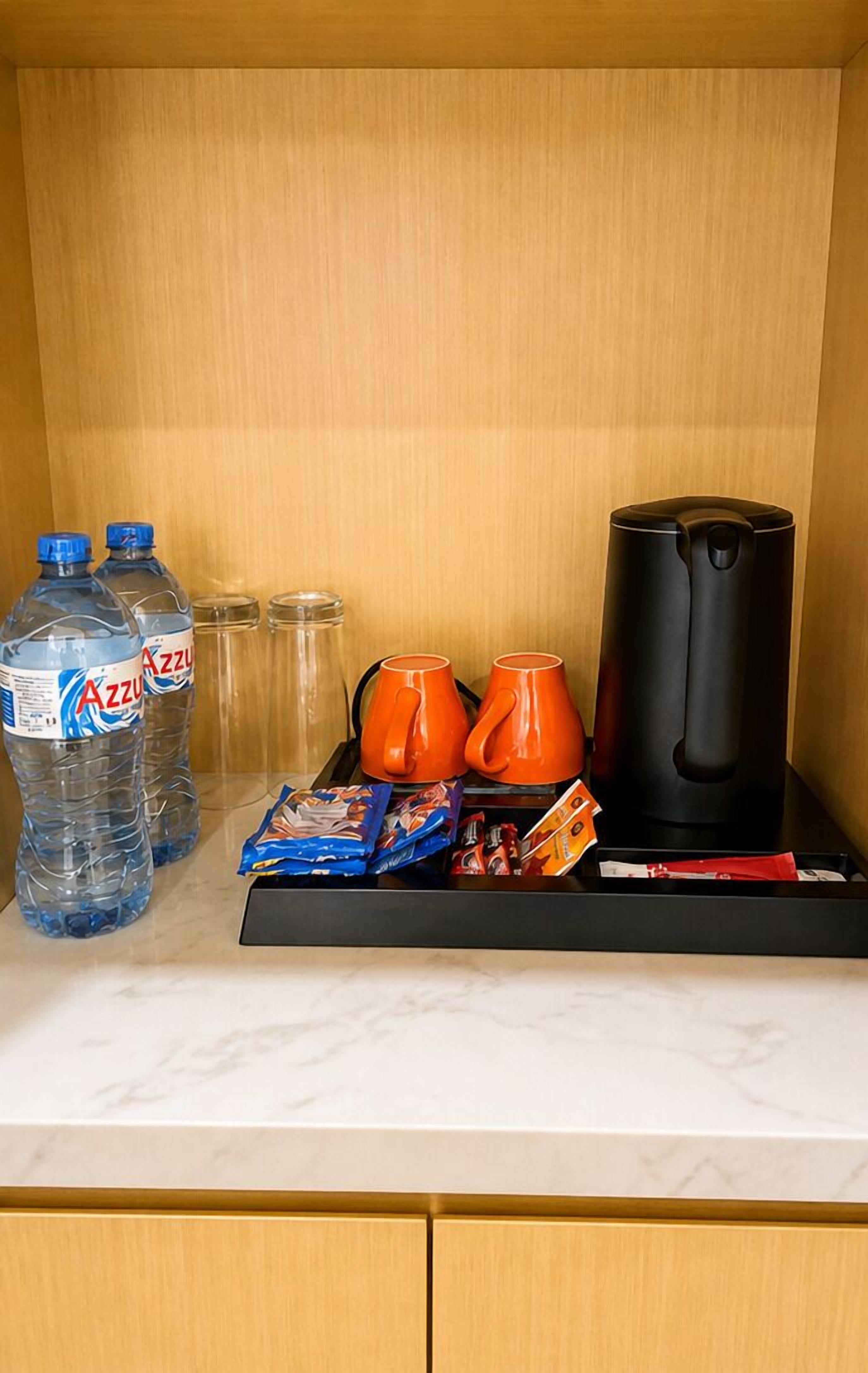 A minibar with bottled water, orange mugs, snacks, and a coffee maker.
