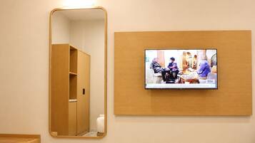 Une pièce comprenant une armoire en bois, un miroir et un téléviseur fixé au mur, qui diffuse une scène avec des personnes.