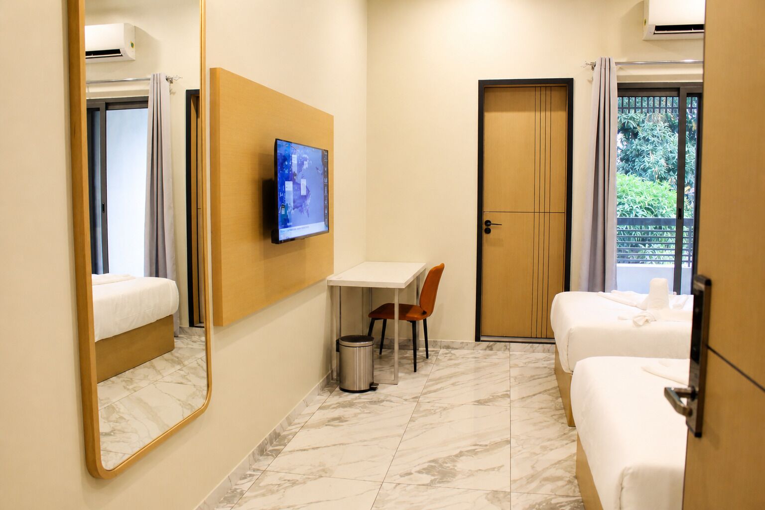 A hotel room with a bed, a desk with a chair, a television, a trash bin, and a door.
