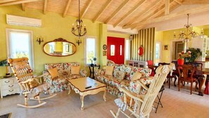 A cozy living room with a sofa, rocking chairs, a coffee table, a dining table with chairs, a chandelier, and a red door. - Villa Avra - Private Garden Pool Oasis in Drama (Drama)