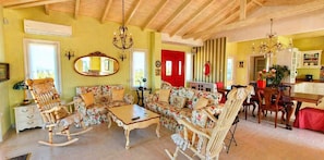 Un salon chaleureux avec un canapé, des fauteuils à bascule, une table basse, une table à manger avec des chaises, un lustre et une porte rouge.