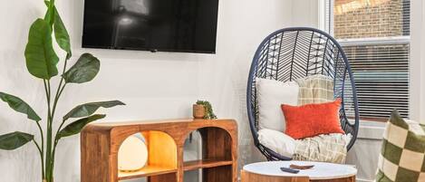 A living room with a wooden console table, a hanging chair, a large plant, and a television mounted on the wall.