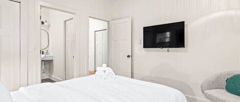 A hotel room with a large bed, a television mounted on the wall, and a chair with a cushion.