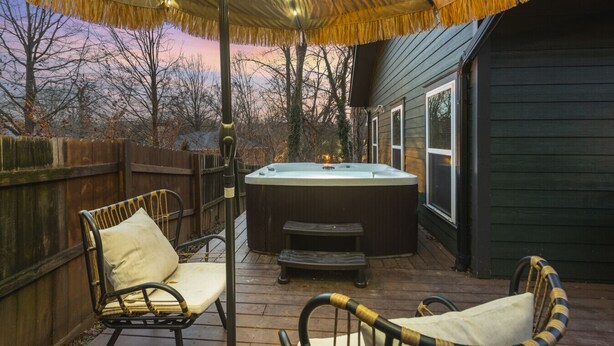 Un espace extérieur avec un jacuzzi, une terrasse en bois, deux fauteuils en osier et un auvent au-dessus.