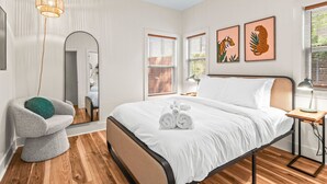Une chambre à coucher moderne avec un lit, une chaise, un miroir et des œuvres d’art accrochées au mur.